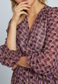 Lila- und braun gemustertes Kleid mit Puffärmel, das ein florales Design und plissierte Textur aufweist. Der glatte Stoff ergänzt die fließende Silhouette.