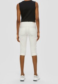 Valkoiset lyhyet farkut käännehelmoilla ja tuplataka-taskuilla, yhdistetty mustan olkaimettoman paidan kanssa, jossa on teksturoitu kangas.