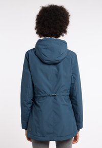 Chaqueta impermeable azul marino con capucha, cintura ajustada y textura suave. Presenta un parche con el logo en la parte inferior de la espalda y un diseño sin costuras.