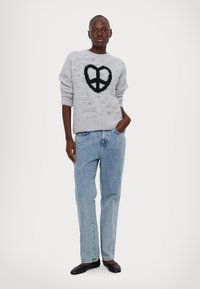 Γκρι πλεκτό πουλόβερ με ένα μαύρο φουργιό σύμβολο ειρήνης, σε συνδυασμό με ανοιχτό μπλε ίσιες τζιν παντελόνες και μαύρες επίπεδες πατούσες.