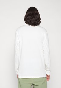 Long-sleeve shirt in white cotton with a crew neck, relaxed fit, and ribbed cuffs. The back view shows a smooth texture and longer hem.