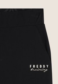 Jogging noir en coton doux avec une taille large. Comprend une poche latérale et un texte réfléchissant "FREDDY training" à l'avant.
