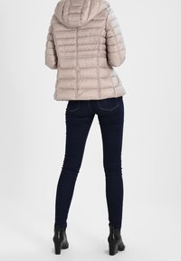 Beige hættetrøje-pufferjakke med quiltet tekstur, lynlås lukning og elastiske manchetter, parret med mørkeblå slim-fit jeans og sorte ankelstøvler.