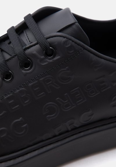 Baskets en cuir noir avec des initiales de marque en relief répétées et des lacets ronds noirs passés dans des œillets en métal.