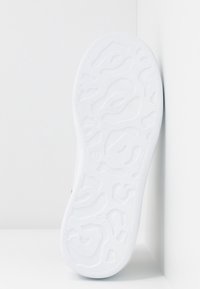 Podešev boty z bílé gumy s texturovaným vzorem vlnitých linií. Hladké okraje a mírné zvýšení u paty.