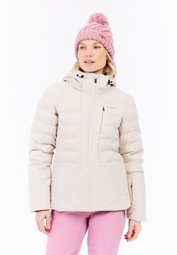 Lichtbeige pufferjack met een capuchon, voorzien van een ritssluiting aan de voorkant en twee zijvakjes. Draagt met een roze gebreide muts met een pompon.