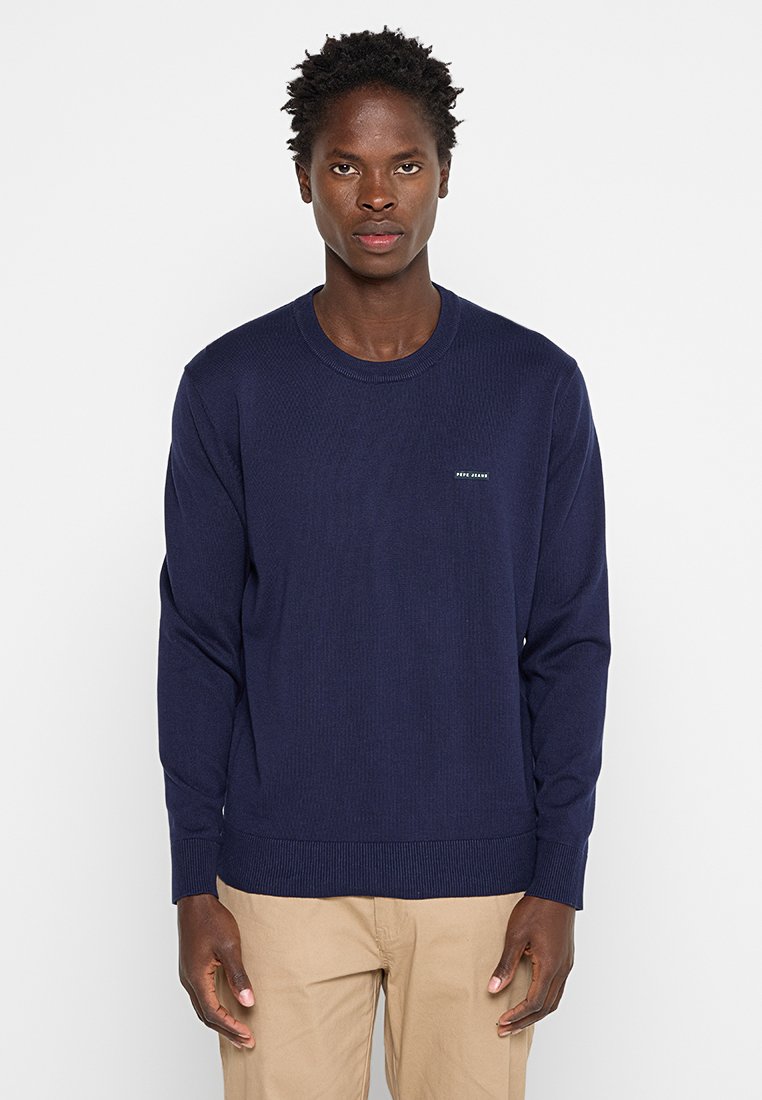 Granatowy prążkowany sweter z długimi rękawami, okrągłym dekoltem i małym logo na piersi. Tkanina jest gładka i lekka.