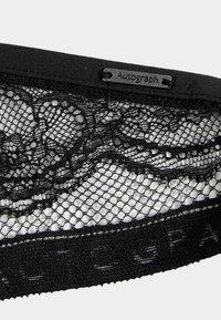 Zwarte kanten bralette met ingewikkelde bloemmotieven, gaasdetails en een gladde onderband met merkaccenten.