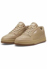 Un paio di sneaker basse beige Puma con design a lacci, punta perforata e loghi del marchio sulla linguetta e sul lato, su sfondo bianco.