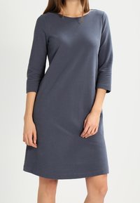 Harmaa, polven kohdalle ulottuva mekko, jossa on pyöreä pääntie ja kolmivartiset hihat. Valmistettu pehmeästä kankaasta, rento malli ja minimaaliset ompeluyksityiskohdat.