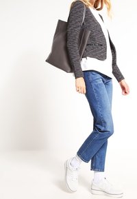 Cardigan gris court à manches longues, haut blanc, jean bleu à jambes droites et baskets blanches, avec un tissu texturé et un sac fourre-tout élégant.