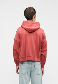 Κόβουν μπορντό cropped hoodie με μεγάλο καπέλο και χαλαρή εφαρμογή, σε συνδυασμό με ανοιχτό μπλε τζιν που διαθέτουν πίσω τσέπες. Λείος υφάσματος, μινιμαλιστικός σχεδιασμός.