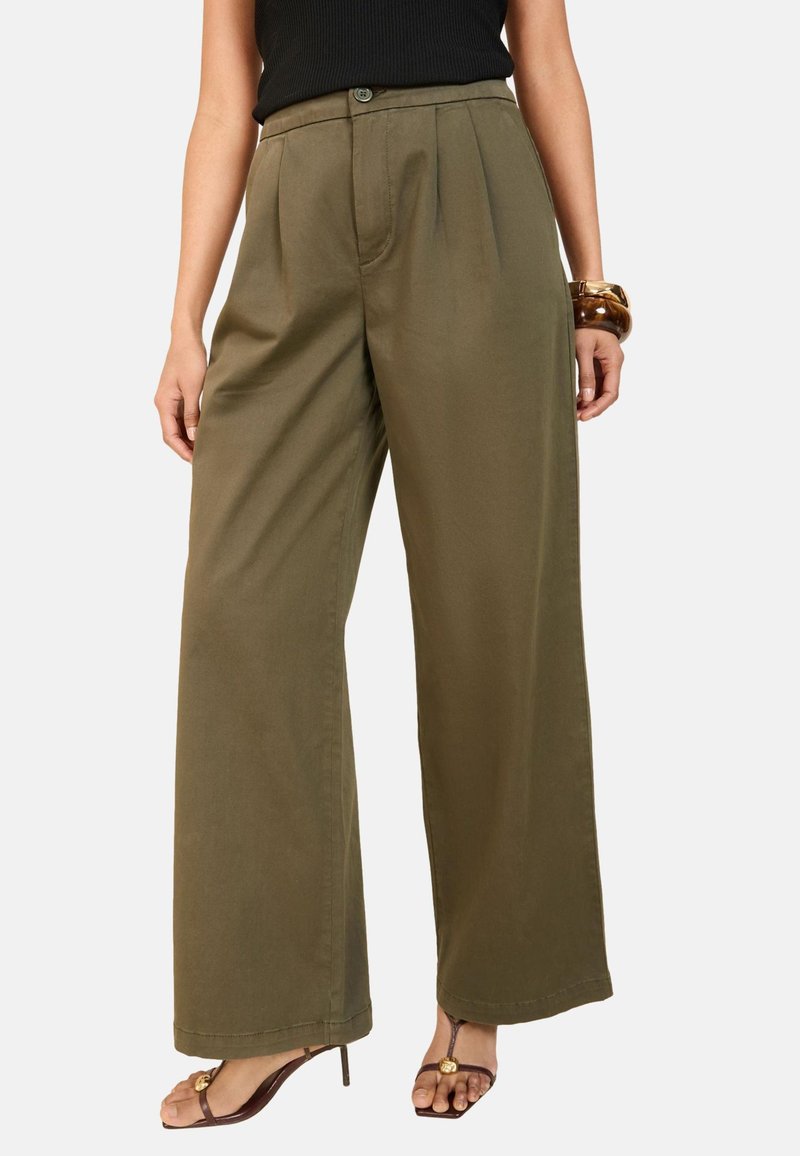 Pantaloni largi de culoare verde măsliniu, cu pliuri, închidere cu nasture și o textură netedă, asortați cu sandale maro cu bretele.