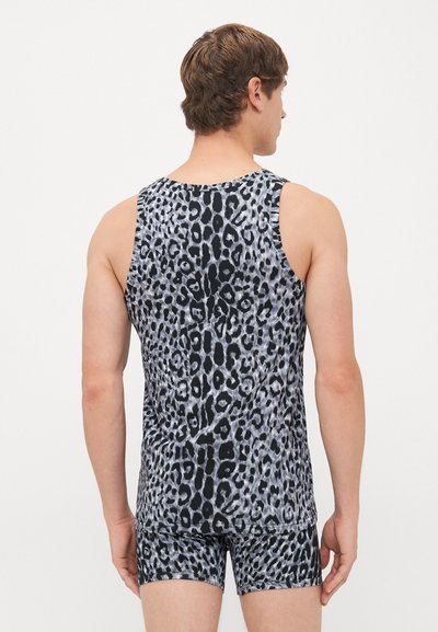 Mann in passendem schwarzem und grauem Leopardenmuster ohne Ärmel und Shorts, stehend mit dem Rücken zu einer schlichten Hintergrund.