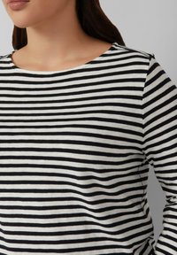 Zwart-witte gestreepte longsleeve top met een ruime halslijn en kleine schouderknopen, met een zachte textuur.