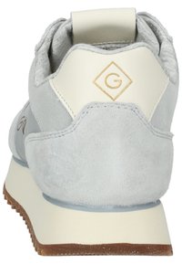 Zapatilla de ante gris con acentos de cuero blanco, que presenta un logo dorado en el talón. Suela gruesa con una textura marrón clara.