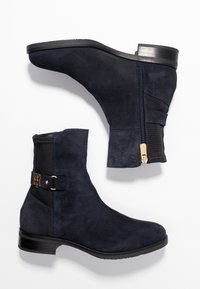 Námořnické modré semišové kotníkové boty s nízkým podpatkem. Mají boční zip, elastickou panel a dekorativní pásek se zlatým akcentem.