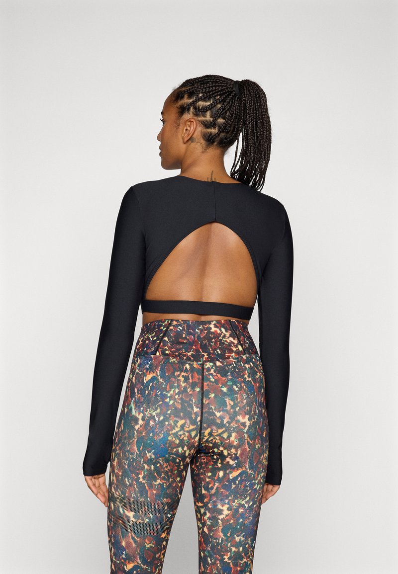 Svart langermet topp med et stort ovalt utsnitt på baksiden, sammen med flerfargede, mønstrede høytaljede leggings med mesh-detaljer.