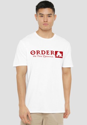 Young man wearing a white T-shirt with red text "Order of the Phoenix" and a phoenix flame logo on chest, standing against a gray background.