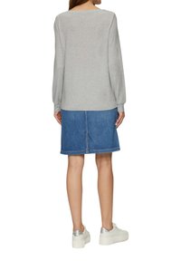 Grijs langwerpig shirt met een ronde halslijn, gecombineerd met een blauwe denim rok die tot halverwege de dij reikt. Model draagt witte schoenen met zilveren accenten.