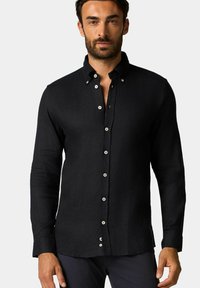 Camicia nera a maniche lunghe con bottoni, realizzata in tessuto testurizzato, caratterizzata da un colletto classico e bottoni bianchi lungo la pattina frontale.