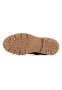 Suela de bota de goma con un dibujo robusto que presenta patrones triangulares y rectangulares; color marrón claro con superficie texturada y bordes estructurados.