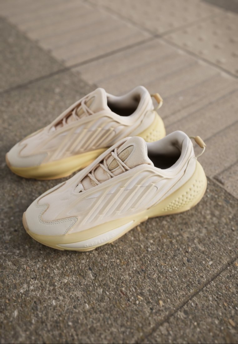 Zapatillas deportivas beige con parte superior de malla y acentos diagonales, suela intermedia texturizada y suela acolchada. Lengüeta trasera para facilitar el calzado.