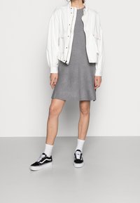 Giacca bomber bianca, vestito grigio fino al ginocchio, scarpe Vans nere, calzini bianchi alla caviglia. Tessuto liscio, vestibilità rilassata e design semplice.