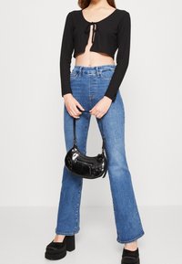Svart ribbad croppad topp med knytning, blå högmidjade jeans och en liten svart lackhandväska. Kraftiga plattformsskor fulländar looken.