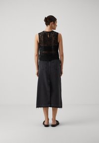 Svart blonde ermeløs topp med nøkkelhull bak, kombinert med en lang svart denimskjørt med frayed hem og to baklommer.