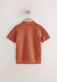 Polo a maniche corte color ruggine lavorata a maglia con motivo strutturato, dotata di colletto e orlo a coste con cuciture a contrasto bianche.