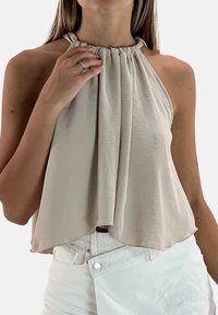 Top beige de tirantes hecho de tela ligera con un escote fruncido y un cuerpo suelto y fluido. Combinado con pantalones blancos de cintura alta.