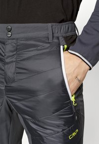 Pantalons isolés gris avec un design matelassé, ceinture élastique, poches zippées avec des accents verts et des détails decouture contrastants.