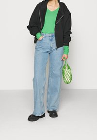 Svart zip-up hoodie, grön v-ringad topp, ljusblå vida jeans, svarta chunky kängor och en grön nätväska. En enkel, avslappnad outfit.