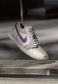 Low-top sneakers featuring a cream leather upper, red accents, gray laces, and a textured white toe box; rubber sole for traction.