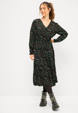 Vestido negro con un patrón de zigzag colorido, mangas largas, escote en V y cintura ceñida. Combinado con botas negras gruesas y cadenas.