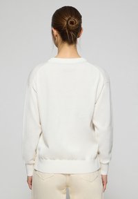 Sweatshirt blanc avec un col rond, des poignets et un ourlet côtelés. Tissu doux avec une texture lisse. Coutures apparentes le long des coutures d'épaule.