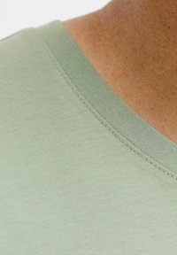 Material de culoare verde deschis, prezentat cu o textură moale și un design cu decolteu în V. Prezintă o cusătură netedă și uniformă de-a lungul gulerului.