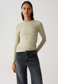 Lichtgroene lange mouw top gemaakt van rekbaar materiaal, gecombineerd met hooggewaisted donkergrijze jeans, die een aansluitende silhouet en een gladde textuur tonen.