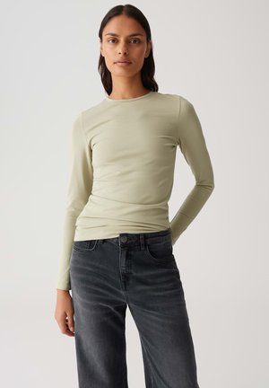Maglietta a maniche lunghe verde chiaro realizzata in tessuto elasticizzato, abbinata a jeans grigio scuro a vita alta, che mostrano una silhouette aderente e una consistenza liscia.