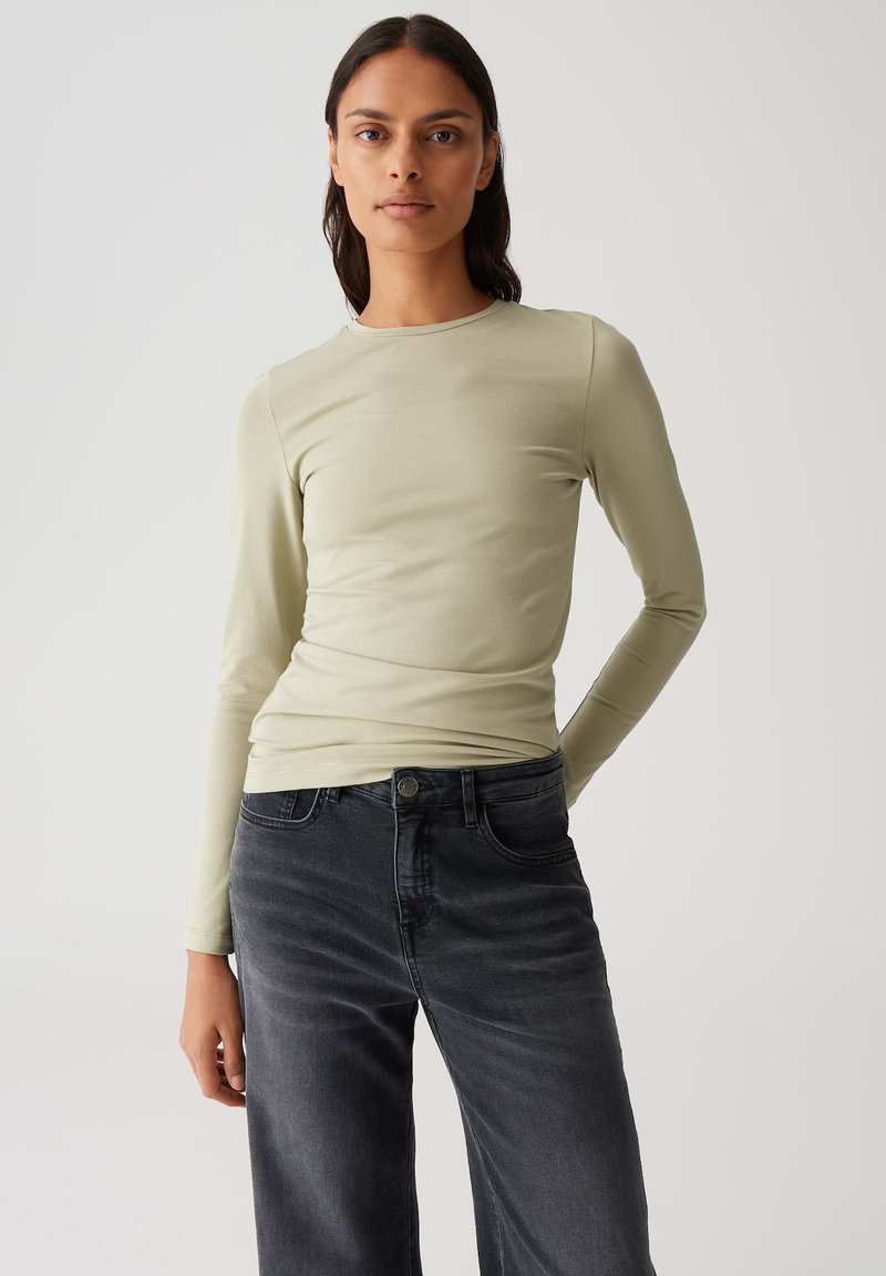 Lichtgroene lange mouw top gemaakt van rekbaar materiaal, gecombineerd met hooggewaisted donkergrijze jeans, die een aansluitende silhouet en een gladde textuur tonen.