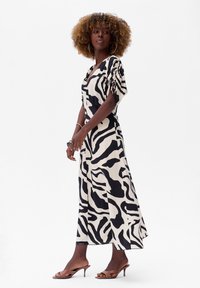 Schwarz-weißer, zebra-muster maxi Kleid mit drapierten Ärmeln, das eine taillierte Taille und einen fließenden Rock hat. Kombiniert mit braunen Sandalen mit Absatz.