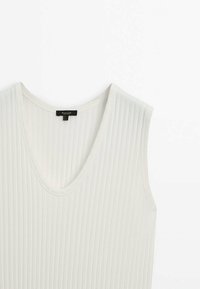 Biała bezrękawnikowa bluzka o ribbowanym wzorze z dekoltem w kształcie litery V i czarną metką wewn�ątrz kołnierza na białym tle.