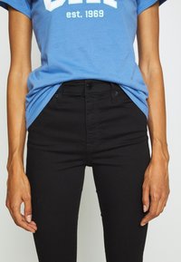Blue cotton t-shirt with white text, paired with black denim jeans featuring a high waist, front pockets, and a smooth texture.