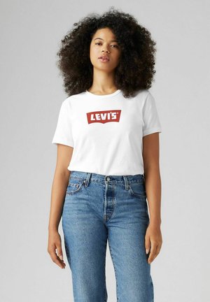 Camiseta de algodón blanca con un logo rojo de Levi's, combinada con unos jeans azules de talle alto. Escote sencillo y mangas cortas, con un corte casual.