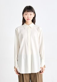 Lange mouwen, ivoorkleurige blouse met een puntige kraag en een verborgen knopenlijst. Gemaakt van een gladde, lichte stof met een ontspannen pasvorm.