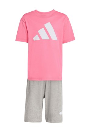 Camisa rosa de manga corta con logo geométrico blanco combinada con pantalones cortos grises hasta la rodilla con un pequeño logo blanco.