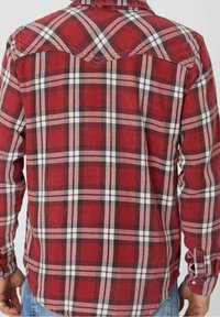 Chemise en flanelle à carreaux rouges avec motifs à carreaux noirs et blancs, poignets à boutons et un empiècement au dos. Tissu texturé.