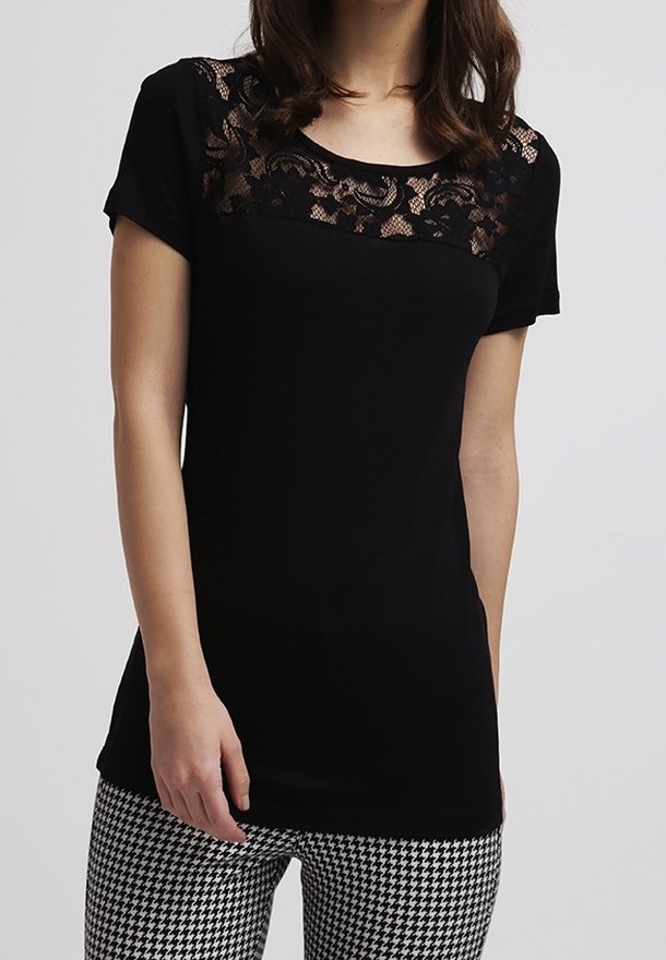 Kvinna iklädd en kortärmad svart topp med spetsdetaljer över bröstet och svart-vita hounds-tooth-byxor.