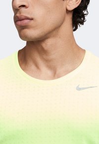 Gros plan sur le bas du visage et le cou d'un homme portant un t-shirt respirant Nike jaune clair avec un dégradé subtil et un logo sur la poitrine.